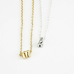 Puede incluir: Dos delicados collares con dijes de iniciales. El collar de la izquierda tiene un dije 'M' de oro, y el collar de la derecha tiene un dije 'K' de plata.