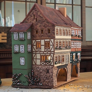 May include: A detailed miniature model of a multi-storey building with a green, white and brown facade. The building has a gabled roof and multiple windows. The model is made of ceramic and has a rustic, hand-painted look.