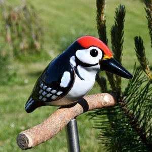 May include: A ceramic woodpecker figurine with black, white, and red paint. The bird is perched on a brown branch with a metal stake.