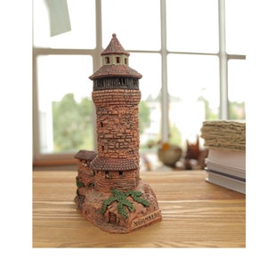 May include: A small, brown ceramic model of a tower with a green roof and the word "NURNBERG" written on the base.
