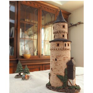 May include: A small, brown, ceramic tower with a black roof and ivy growing on the side. The tower has several windows and is sitting on a white surface.