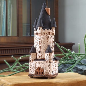 May include: A hand-crafted ceramic tower with a black roof and white stone walls. The tower has a small door and windows, and is decorated with details like a flag and a pointed spire.