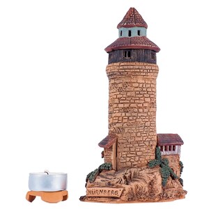 May include: A ceramic model of a tower with a brown roof and stone walls. The tower is labeled "NURNBERG". A small, silver candle holder is in the foreground.
