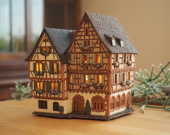 May include: A ceramic model of a traditional German half-timbered house with a brown roof, white walls, and windows with shutters. The house has a small porch with a door and two windows. The house is illuminated with small lights inside.