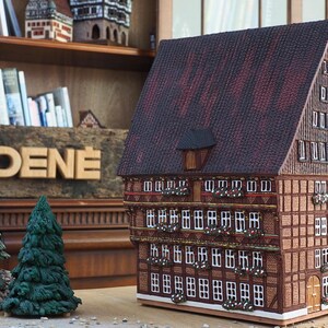 Puede incluir: Un modelo detallado de una casa tradicional alemana de entramado de madera con techo marr&oacute;n, ventanas blancas y vigas de madera decorativas. El modelo est&aacute; hecho de madera y tiene un letrero que dice "MIDENE".