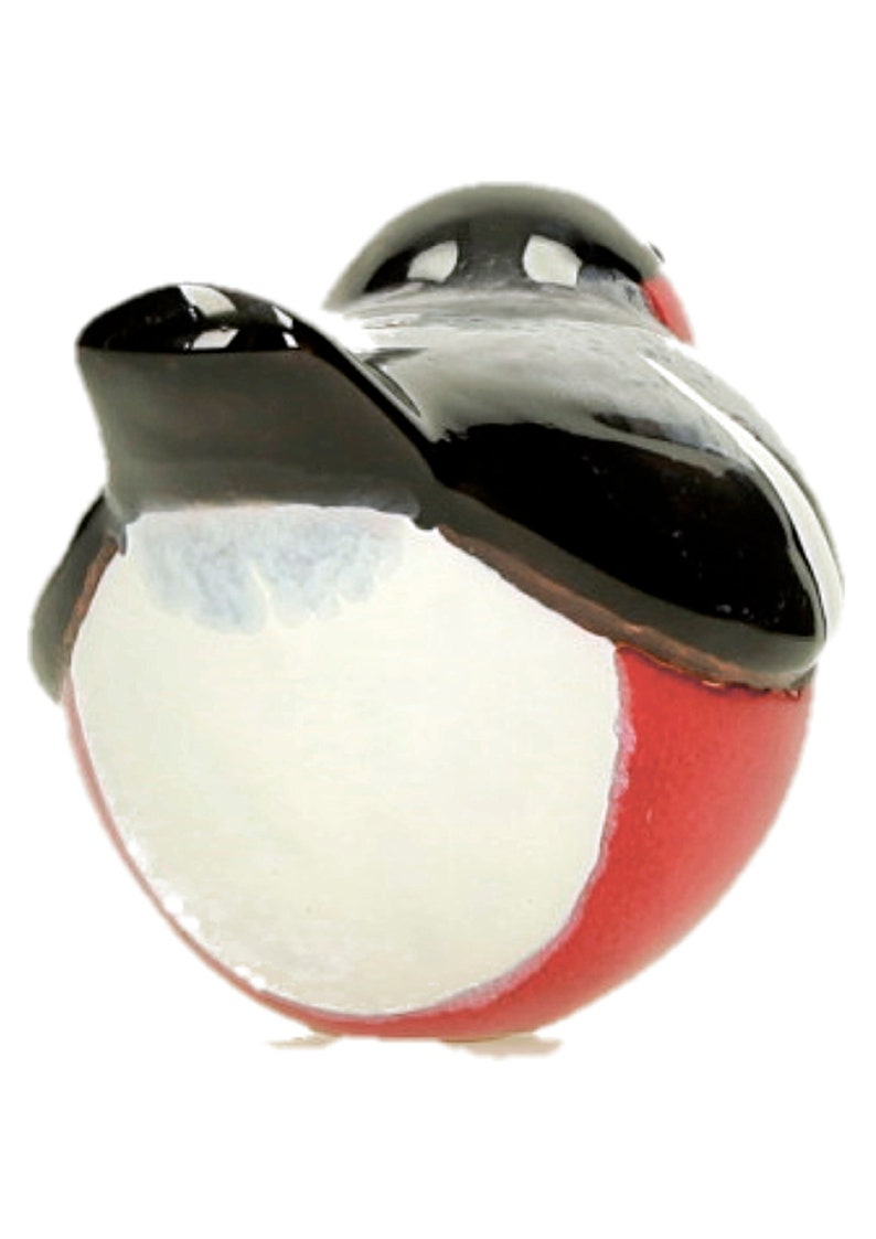 May include: A ceramic robin figurine with a black head and wings, a white belly, and a red breast. The robin is facing away from the camera and is perched on a white surface.