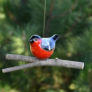 May include: A ceramic bird ornament with a red body, black head, and blue wings, perched on a branch.