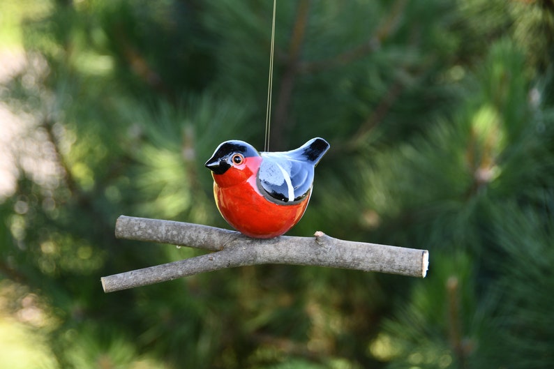 May include: A ceramic bird ornament with a red body, black head, and blue wings, perched on a branch.