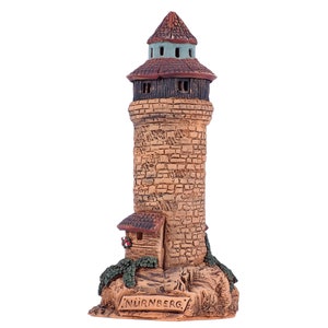 May include: A ceramic model of a tower with a brown roof and a small house at the base. The tower is made to look like stone and has a sign that reads "NURNBERG".