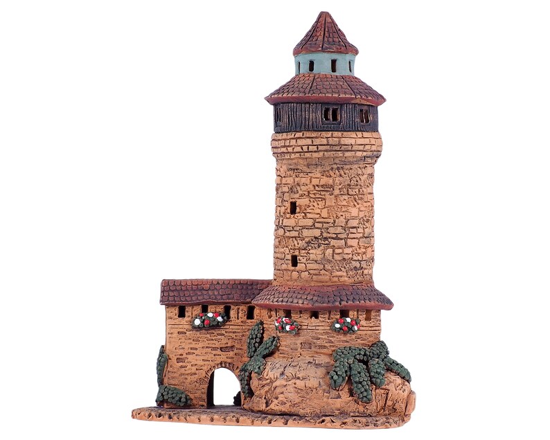 May include: A small, hand-crafted ceramic tower with a brown roof and stone walls. The tower has a small arched doorway and is decorated with green vines and red flowers.