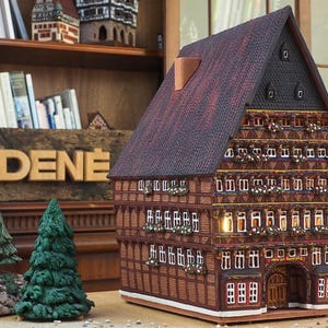 Puede incluir: Un modelo detallado de una casa tradicional alemana de entramado de madera con un techo de tejas rojas y un letrero que dice "MIDENE". La casa est&aacute; decorada con detalles intrincados y tiene m&uacute;ltiples ventanas.