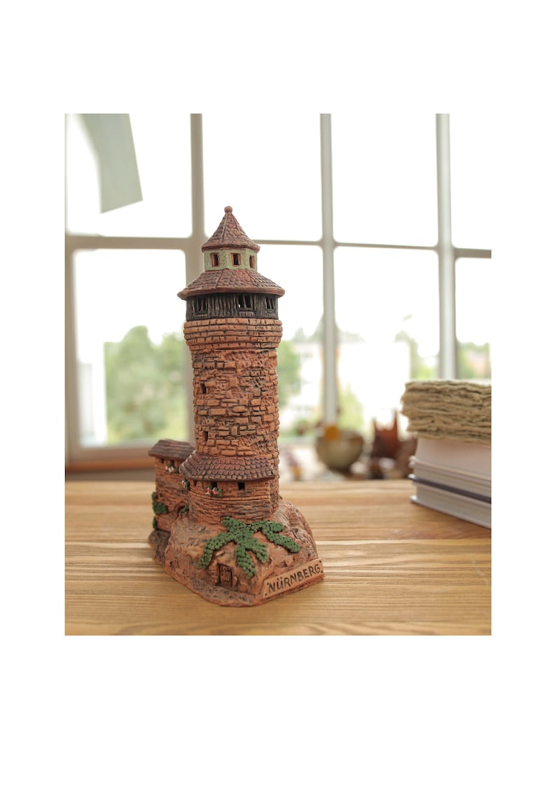 May include: A small, brown ceramic model of a tower with a green roof and the word "NURNBERG" written on the base.