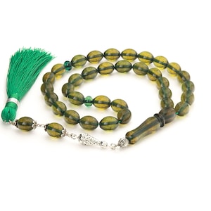 Peut inclure: Un collier de prière en ambre vert avec un pendentif en argent et un pompon vert. Les perles sont de forme ovale et de couleur vert foncé.