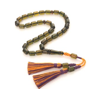 Puede incluir: Un collar de cuentas de oración de ámbar verde con un borla de madera y dos borlas moradas y naranjas.