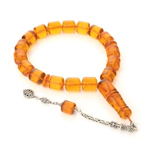 May include: A traditional amber prayer beads necklace with a silver tassel. The beads are a rich, warm amber colour and are strung on a silver chain.