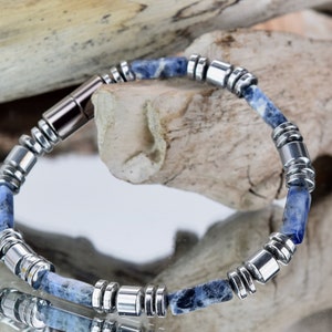 Peut inclure: Un bracelet bleu et argent avec un fermoir magnétique. Le bracelet est composé de petites perles rondes et a une pierre bleue au centre de chaque perle.