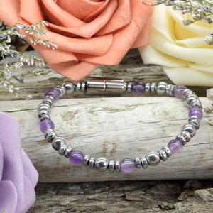 May include: A purple amethyst and silver magnetic bracelet. The bracelet is made with small round beads and has a magnetic clasp.