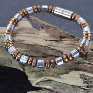 Pode incluir: Um bracelete magnético de prata e cobre com fecho. O bracelete é feito de pequenas contas redondas.