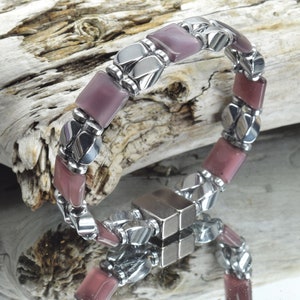 May include: A silver and purple magnetic bracelet with square-shaped purple stones. The bracelet has a magnetic clasp.