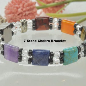 Peut inclure: Un bracelet chakra à 7 pierres avec de l'améthyste, du lapis-lazuli, de la turquoise et d'autres pierres. Le bracelet est fait de perles claires et noires et a un fermoir magnétique.