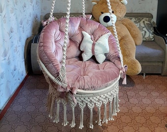 A charming macrame hanging hammock chair with a butterfly pattern on the back, soft pink cushions and fabric bow ties