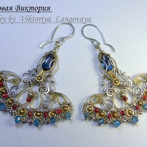 May include: A pair of silver and gold wire earrings with blue and red gemstones. The earrings are in the shape of a fan and have a delicate, intricate design.