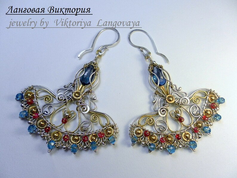 May include: A pair of silver and gold wire earrings with blue and red gemstones. The earrings are in the shape of a fan and have a delicate, intricate design.