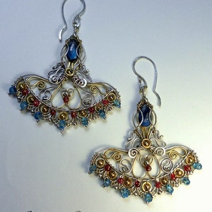 May include: A pair of silver and gold earrings with blue and red gemstones. The earrings are in the shape of a fan and have a delicate, intricate design. The earrings are labeled "jewelry by Viktoriya Langovaya".