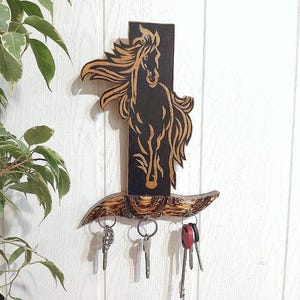 May include: Wooden key holder featuring a black and brown silhouette of a horse. The horse is running with a flowing mane. The key holder has five hooks for hanging keys.