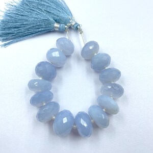 Könnte beinhalten: Eine Kette aus hellblauen, facettierten Edelsteinperlen mit einer passenden blauen Quaste. Die oval geformten Perlen sind aufgefädelt. Die Quaste besteht aus weichen, hellblauen Fäden, was einen zarten und eleganten Look ergibt.