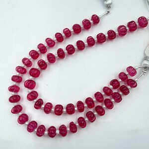 May include: A double-strand necklace featuring carved, ribbed, deep pink beads alternating with small, round, white seed beads. The necklace is finished with silver-toned metal hardware and white tassels at the ends of the strands.