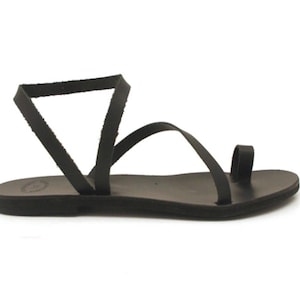 May include: Black leather sandal with a toe loop and ankle strap. The sandal features a flat sole and a minimalist design, perfect for warm weather. The sandal is shown on a white background.