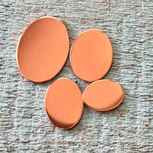 May include: Four copper-colored metal discs in various oval shapes. The discs are smooth and shiny.