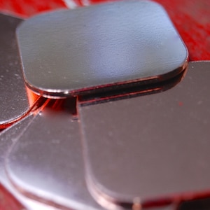 May include: A stack of four square copper heat sinks, likely used for cooling electronic components. The heat sinks are shiny and have a metallic finish.