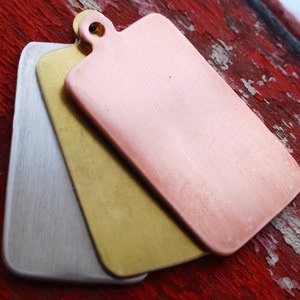 May include: Three rectangular metal tags in silver, gold, and copper. The tags are stacked on top of each other, with the copper tag on top.