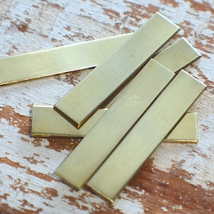 May include: A set of six brass rectangular metal bars, stacked on top of each other. The bars are smooth and have a shiny finish.