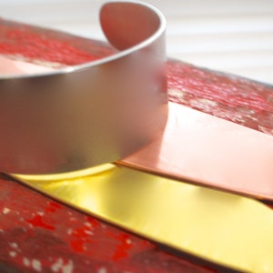 May include: A silver bangle bracelet with a smooth, shiny finish. The bracelet is stacked on top of a pink and gold bangle bracelet.