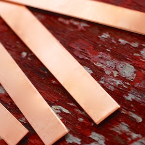 May include: Four thin strips of copper metal arranged in a diagonal pattern on a red, weathered wooden surface.