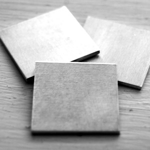 May include: Three silver metal squares, each with a smooth, slightly textured surface.