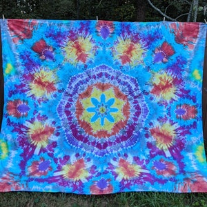 May include: A large, colorful tie-dye tapestry with a circular pattern in shades of blue, purple, red, yellow, and white.