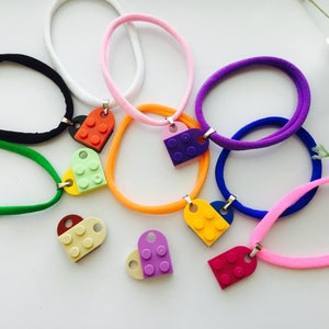 May include: A set of colorful hair ties with heart-shaped charms made from Lego bricks. The charms are in various colors, including red, green, yellow, purple, and blue.