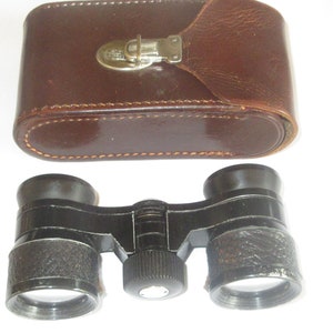 May include: Black binoculars with a leather carrying case. The binoculars have a textured finish and a central focus knob.