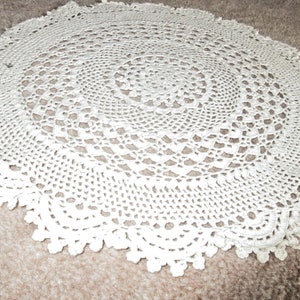 Può includere: Tovaglietta all'uncinetto bianca con un design circolare. La tovaglietta ha un motivo delicato e traforato e un bordo a festoni.