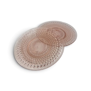 May include: Two round, translucent pink glass plates featuring a textured hobnail pattern along the outer rim and a central sunburst design with radiating lines. The plates are stacked slightly offset, showcasing the pressed glass construction.