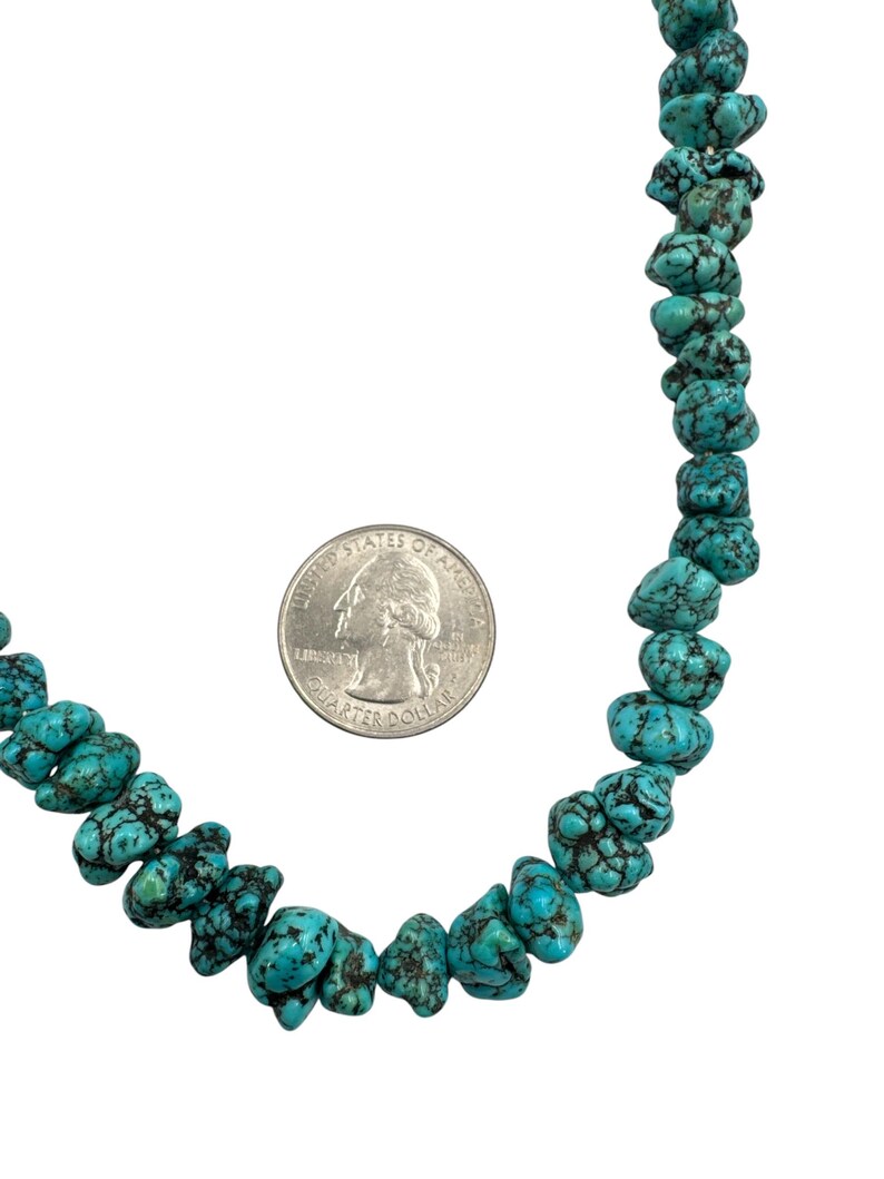 Puede incluir: Un collar hecho de cuentas de turquesa irregulares y pulidas con vetas de matriz oscura. Una moneda de veinticinco centavos de los Estados Unidos se coloca junto a las cuentas para proporcionar una referencia visual del tama&ntilde;o de las piedras.