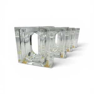 May include: A set of clear, square-shaped glass drinking glasses. Each glass has a rectangular body with a rounded handle and a small, gold-colored base. The glasses are arranged in a row, showcasing their design.