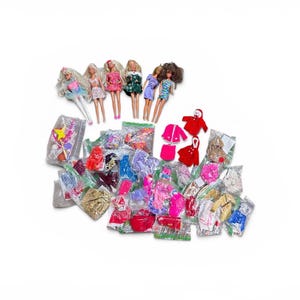 Op de afbeelding: Een verzameling van zes modepoppen met verschillende haarkleuren en outfits, vergezeld door een groot assortiment poppenkleding en accessoires verpakt in talloze doorzichtige plastic zakjes, met items in de kleuren rood, roze, blauw en goud.