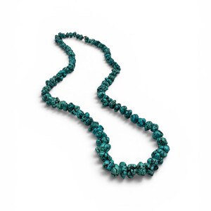 Puede incluir: Un collar de una sola hebra compuesto por numerosas cuentas de turquesa irregulares con forma de pepita. Las cuentas presentan un color azul turquesa vibrante con vetas de matriz negra prominentes, ensartadas en un bucle continuo.