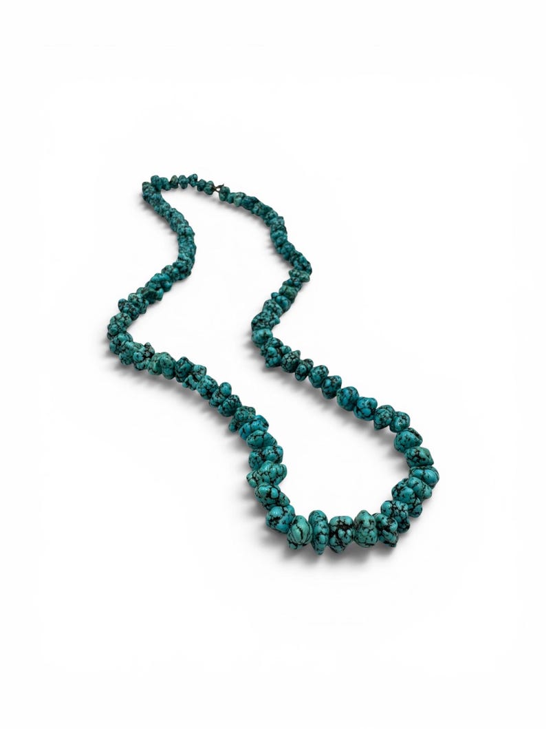 Puede incluir: Un collar de una sola hebra compuesto por numerosas cuentas de turquesa irregulares con forma de pepita. Las cuentas presentan un color azul turquesa vibrante con vetas de matriz negra prominentes, ensartadas en un bucle continuo.