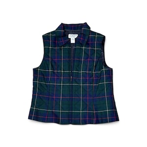 May include: A sleeveless quilted vest featuring a dark green, navy blue, and red plaid pattern with thin white grid lines. The vest has a full-length front zipper, a pointed collar, and a white interior label with the text Pendleton.